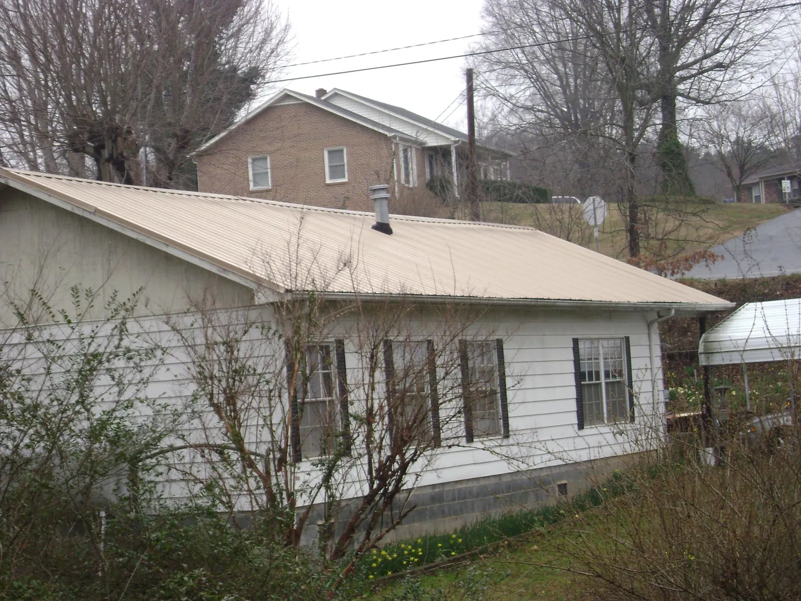 Tan metal roof on a white sided house set into a hillside — Commercial Roofing by Roofing Brothers in Jamestown